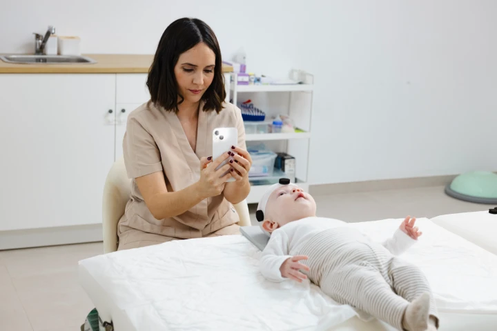 Vista de frente de cómo mide la fisio pediátrica con el móvil en la mano y el bebé en posición