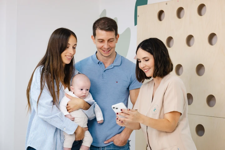 Familia feliz con bebé en brazos mientras fisioterapeuta pediátrica les explica los resultados de la medición con CraniaMed