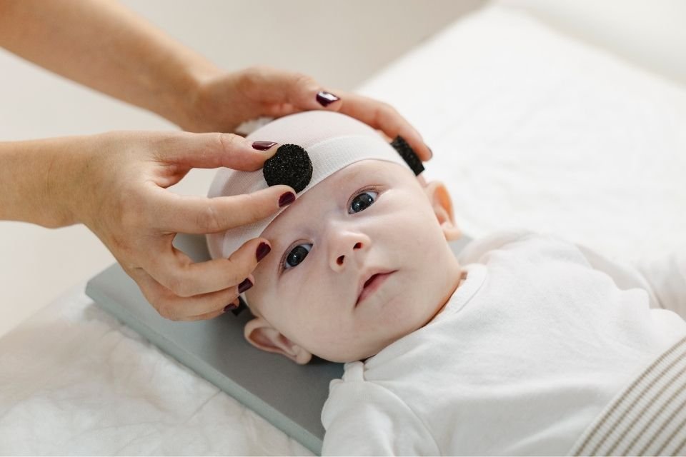 Primer plano de un bebé mientras las manos de una fisio pediátrica le colocan el marcador frontal