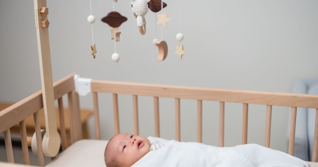 Bebé en la cuna tumbado boca arriba mirando un juguete